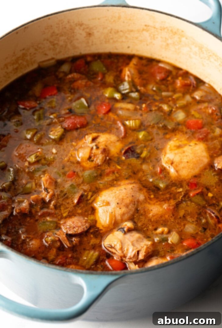 Louisiana Classic Gumbo 7 Whole pieces of chicken thigh simmering in a large pot with a rich, dark broth, alongside vegetables and spices.