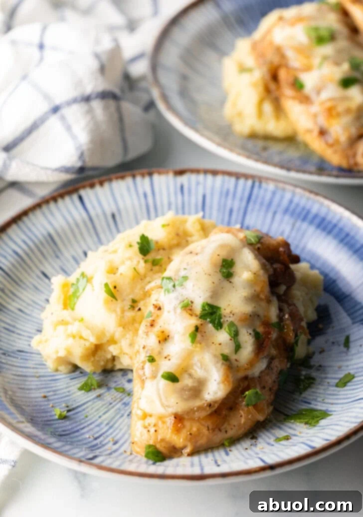 Plate of mashed potatoes topped with French onion chicken breast and gravy.