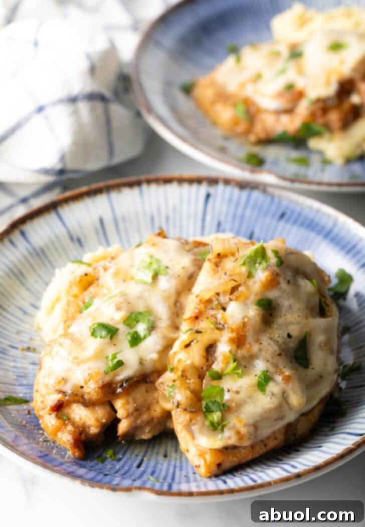 Plate of mashed potatoes topped with 2 French onion chicken breasts and gravy.