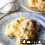 Plate of mashed potatoes topped with French onion chicken breast and gravy.