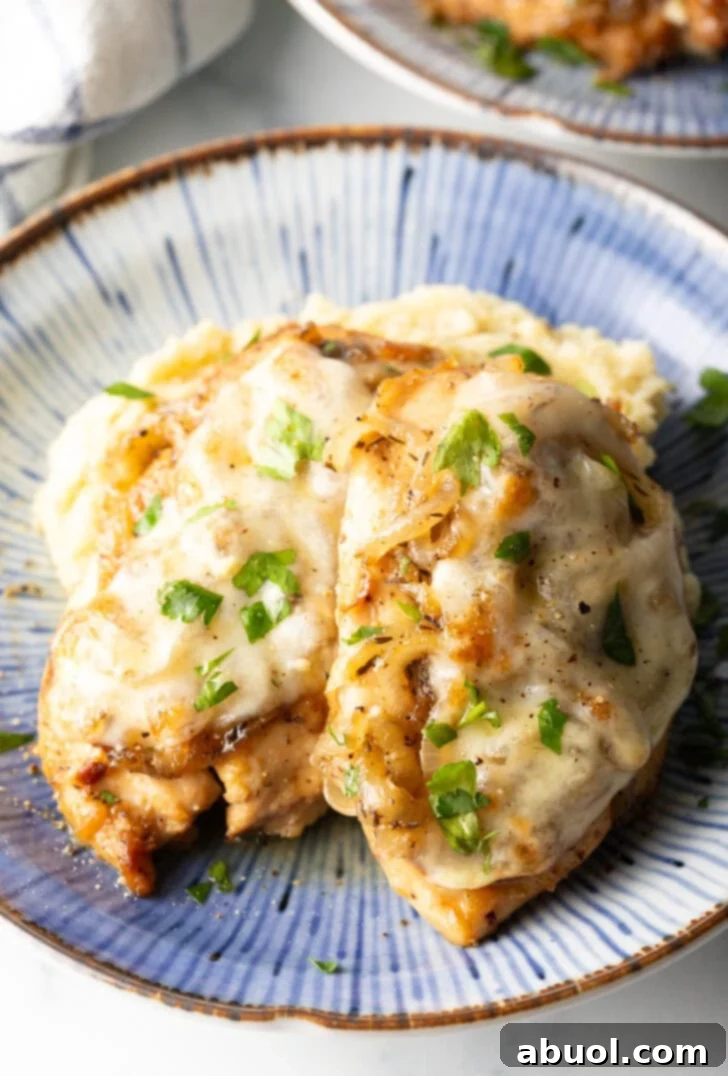 Plate of mashed potatoes topped with 2 French onion chicken breasts and gravy.