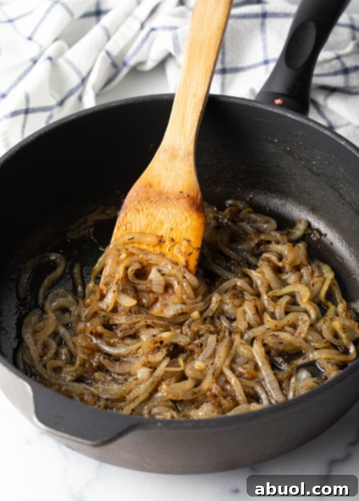 Caramelizing onions in a black skillet with wooden spatula.