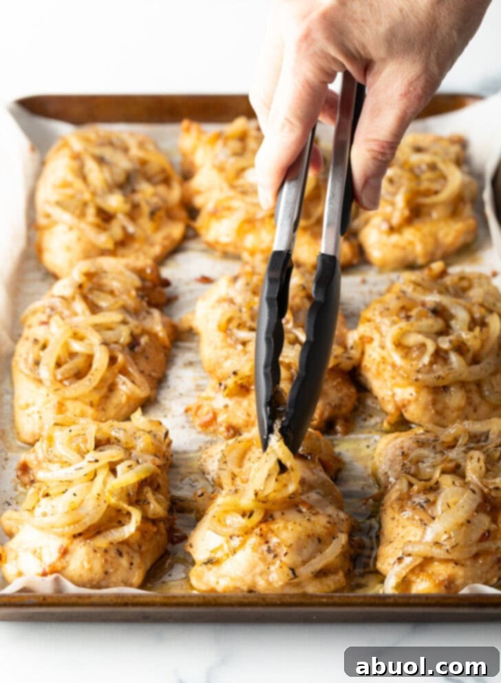 Hands with tongs adding caramelized onions to the tops of chicken on a baking sheet.