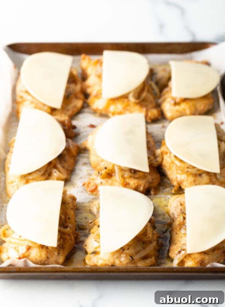 9 chicken thighs on a baking sheet topped with unmelted provolone cheese.