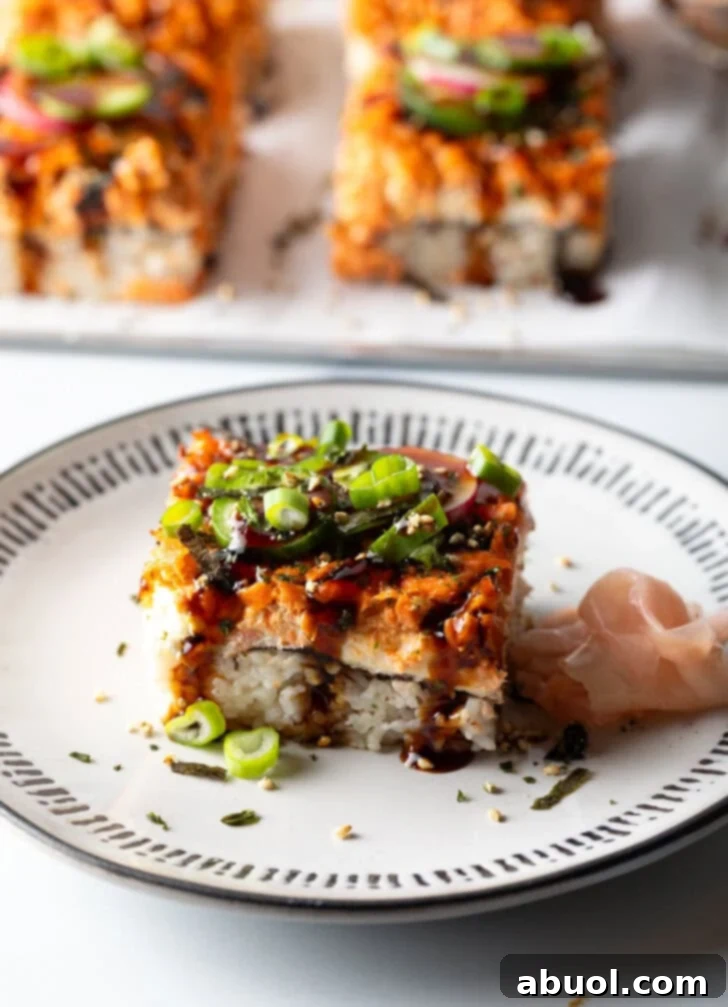 Square of sushi bake on a white plate, garnished with fresh green onions and sesame seeds.