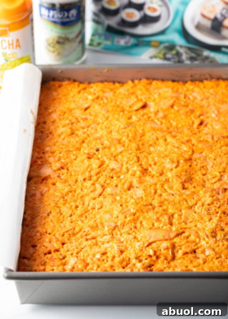 The fully assembled salmon sushi bake, with its vibrant top layer of salmon mixture, pressed into a rectangular baking pan and ready for the final bake.