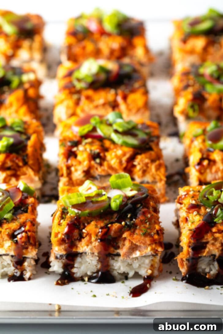 Rows of perfectly sliced squares of salmon sushi bake arranged neatly on a baking sheet, showcasing its enticing layers and garnishes.