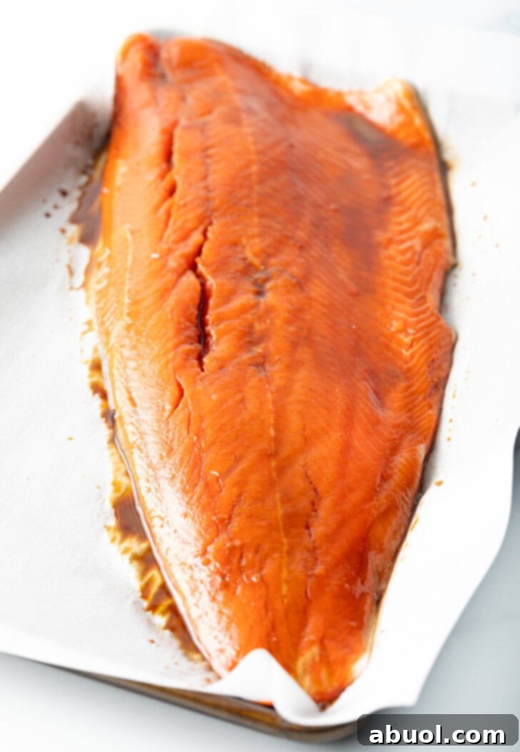 Side view of a perfectly cooked salmon fillet on parchment paper, seasoned with soy sauce and ready to be flaked.