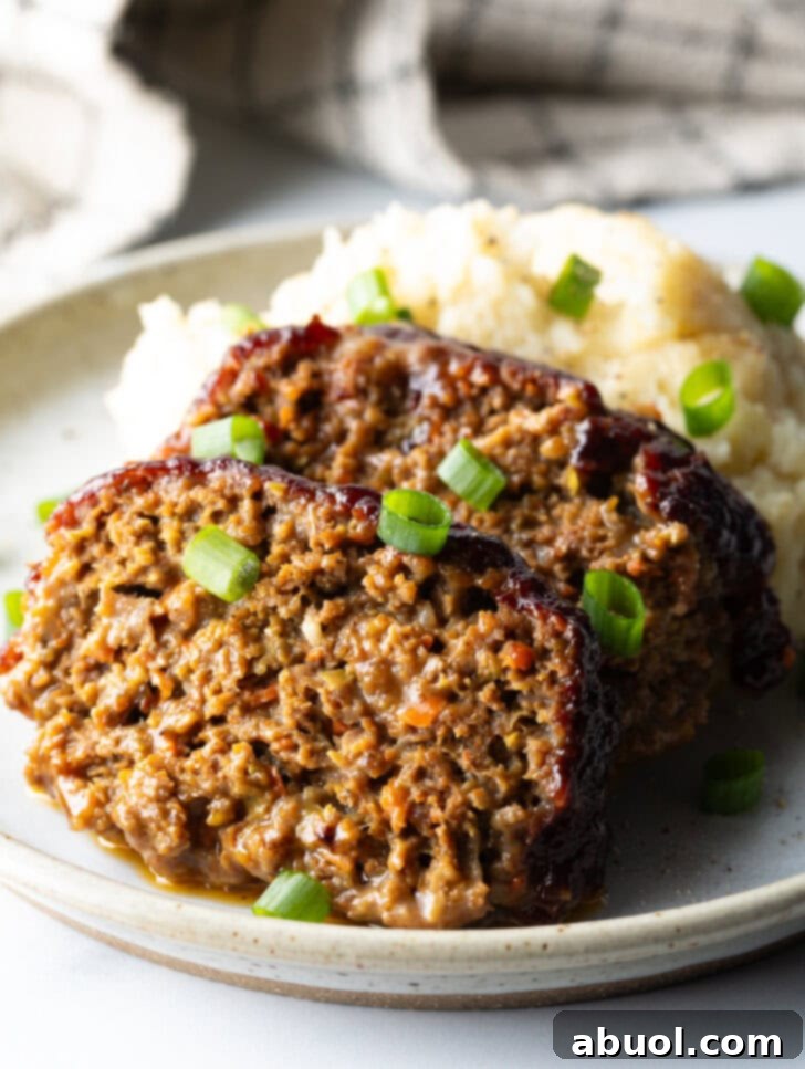 Slow Smoked Meatloaf 2 Two generous slices of smoked meatloaf, perfectly browned, resting on a pristine white plate beside a creamy scoop of mashed potatoes. Freshly chopped green onions provide a vibrant garnish, hinting at the savory depth of this comfort food classic.