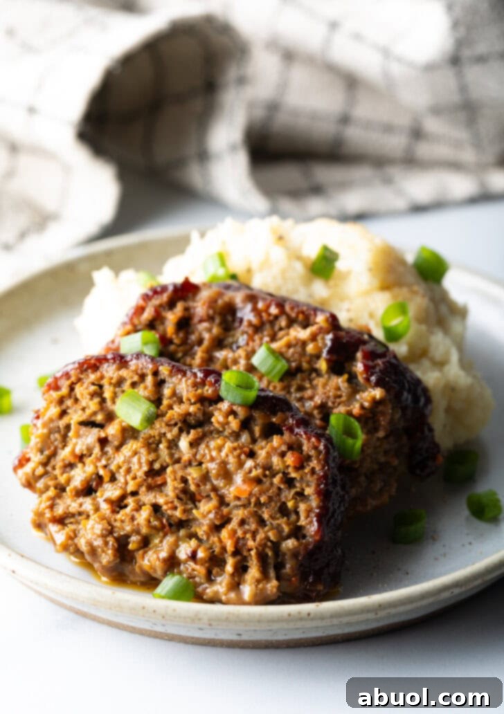 Slow Smoked Meatloaf 12 Two enticing slices of smoked meatloaf artfully arranged on a white plate, accompanied by a generous scoop of creamy mashed potatoes. The entire dish is garnished with finely chopped green onions, ready to be enjoyed as a hearty and comforting meal.