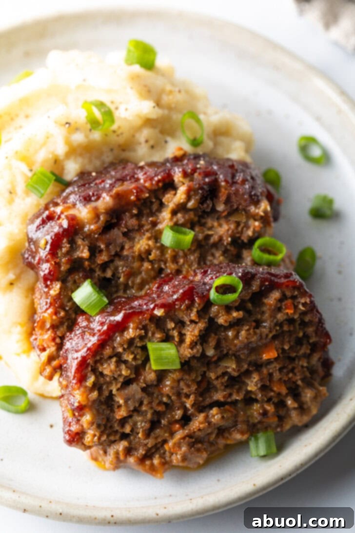 Slow Smoked Meatloaf 13 Two slices of smoked meatloaf, artfully plated with a dollop of creamy mashed potatoes and garnished with fresh green onions, showcasing a perfectly cooked and glazed finish.