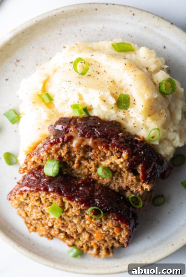 Slow Smoked Meatloaf 3 Two slices of perfectly cooked smoked meatloaf, glistening with barbecue glaze, served on a white plate alongside a fluffy mound of mashed potatoes. A sprinkle of fresh green onions adds color and a delicate bite to this hearty meal.
