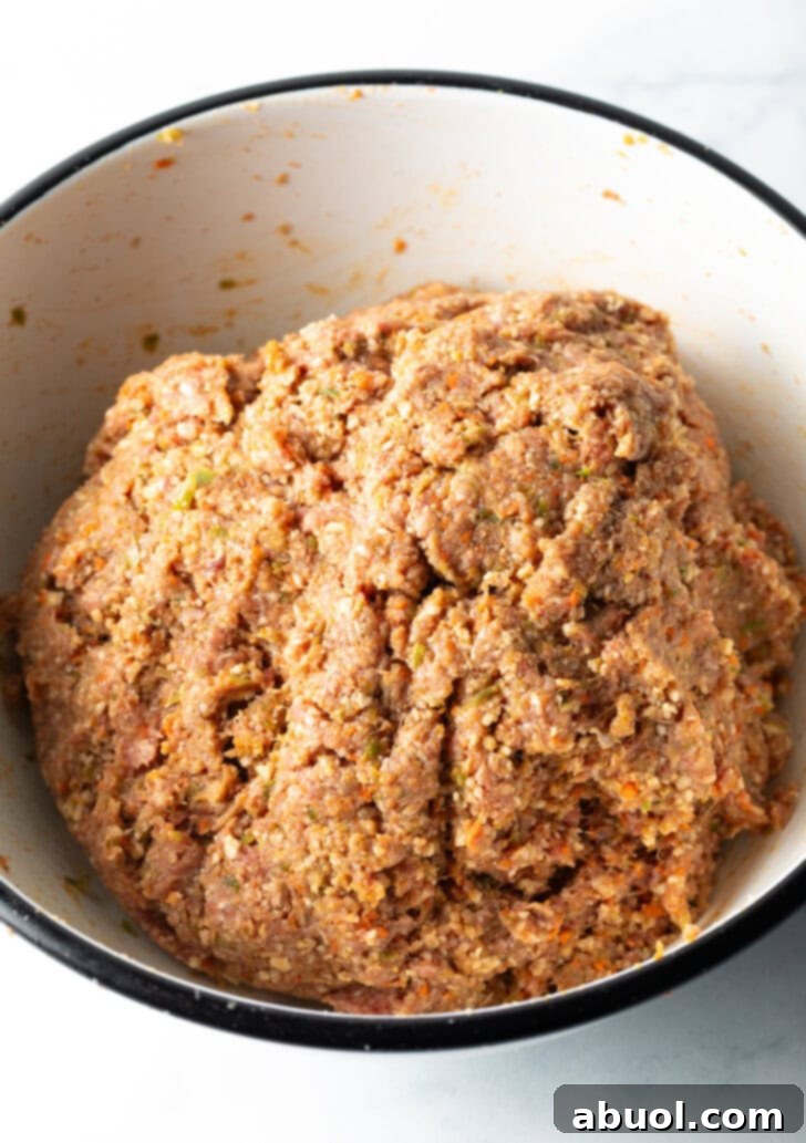 Slow Smoked Meatloaf 8 A hand gently but thoroughly mixing the meatloaf ingredients in a large bowl. The mixture is uniform, showcasing the perfect blend of ground beef, pureed vegetables, and spices, ensuring a moist and flavorful result.