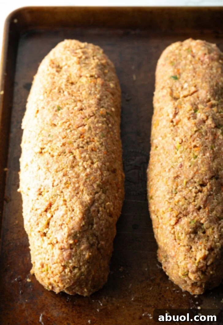 Slow Smoked Meatloaf 9 Two perfectly formed, raw meatloaves placed side-by-side on a rimmed baking sheet, brushed generously with barbecue sauce, ready for the smoker. The glaze hints at the delicious crust to come.