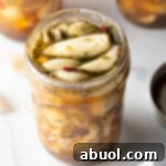 Top down open glass jar stuffed with preserved garlic and herbs.