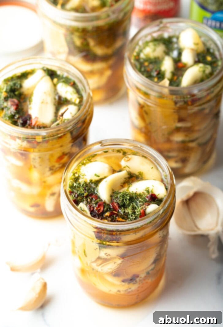 Top down open glass jar stuffed with preserved garlic and herbs.