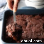 Hand using a metal spoon to scoop a serving of pudding cake from the baking pan.