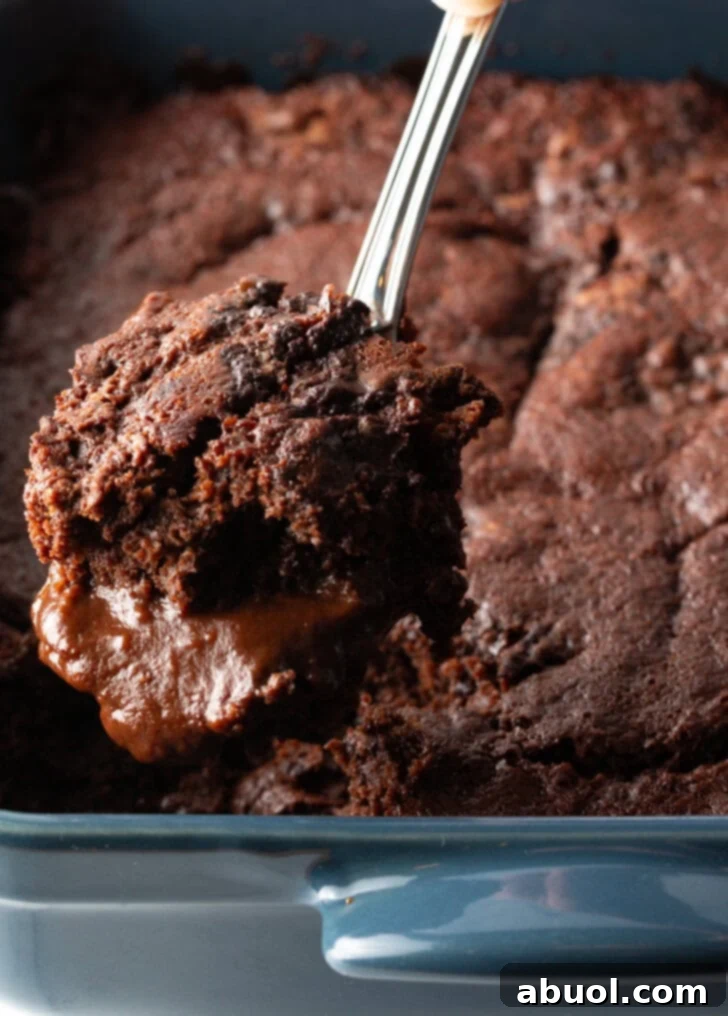 Hand using a metal spoon to scoop a serving of pudding cake from the baking pan.