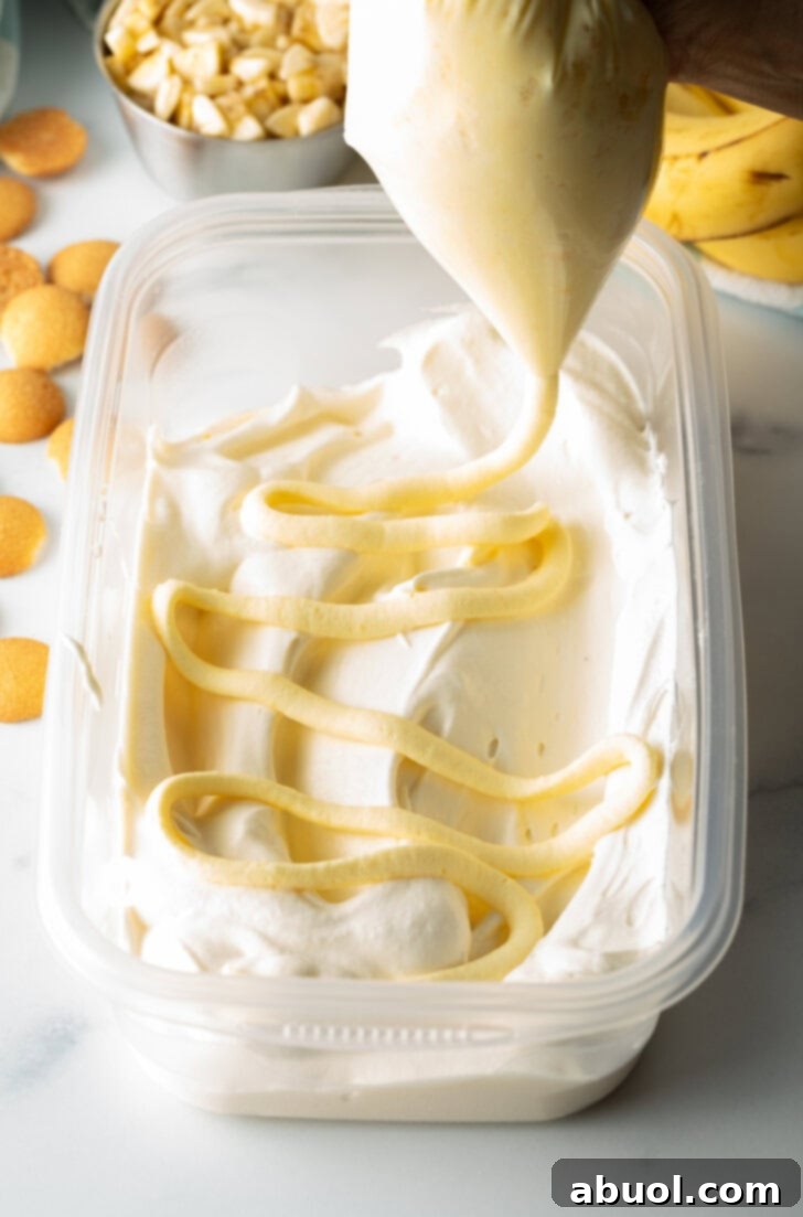 No-Churn Banana Pudding Dream 7 Squeezing banana pudding from a piping bag over the frozen ice cream in a rectangle container.