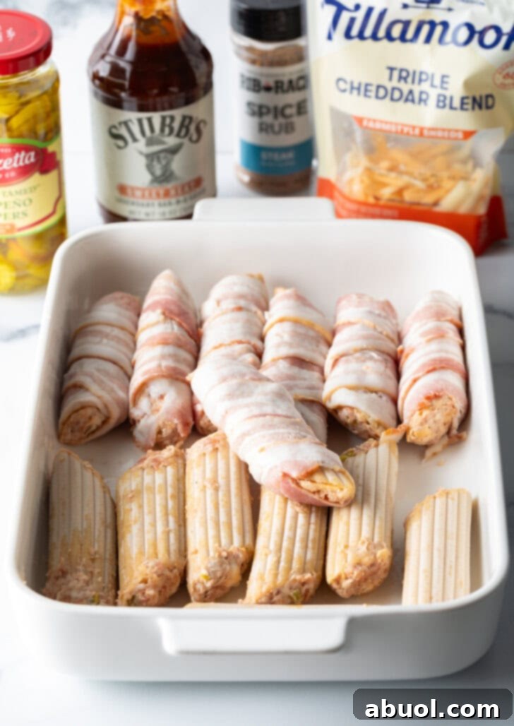 White baking dish with two rows of meat and cheese stuffed manicotti. Half of the pasta is wrapped in pieces of raw bacon.