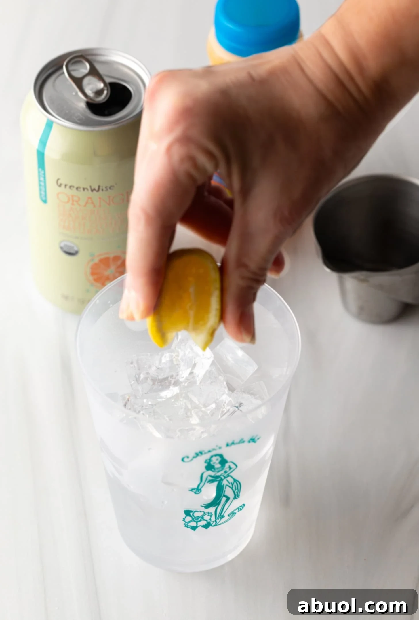 A hand squeezing a fresh orange into a glass filled with ice and other liquids.