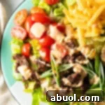 Big mac burger salad with shredded lettuce, ground beef, halved grape tomatoes, shredded cheese, pickles, and sliced green onion, all topped with a drizzle of Thousand island dressing, presented as a delicious and complete meal.