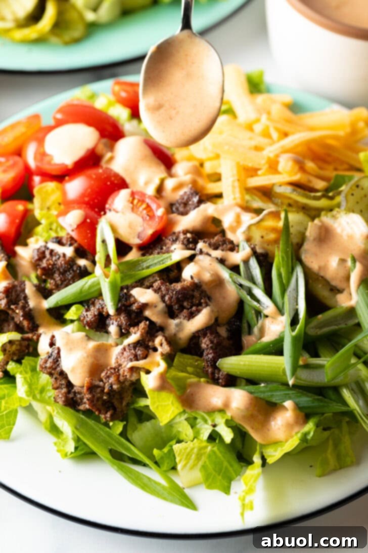 A spoon generously drizzling creamy, golden Big Mac sauce over the vibrant burger salad, highlighting the rich texture of the sauce and its visual appeal.