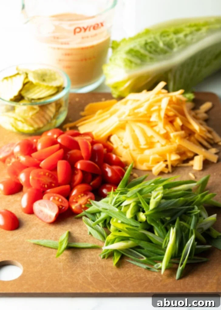 Recipe ingredients neatly arranged on a cutting board: Piles of vibrant shredded cheese, bright halved cherry tomatoes, finely sliced green onions, and a small glass of tangy pickle slices, all meticulously prepped for the Big Mac Salad.