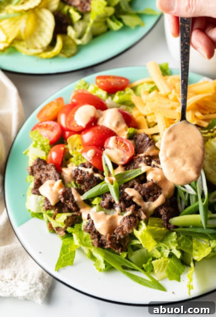 A close-up of a spoon artfully drizzling the thick, creamy, and flavorful Big Mac sauce over a fresh and colorful burger salad, showcasing its perfect consistency.
