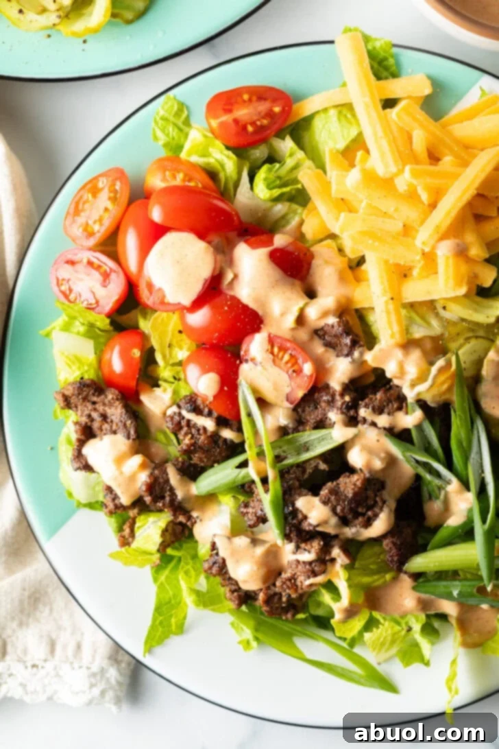 A vibrant Big Mac burger salad on a white plate, showcasing shredded lettuce, well-cooked ground beef, halved grape tomatoes, generous shredded cheese, crisp pickles, and finely sliced green onion, all brought together with a creamy drizzle of Thousand Island dressing for a complete meal.