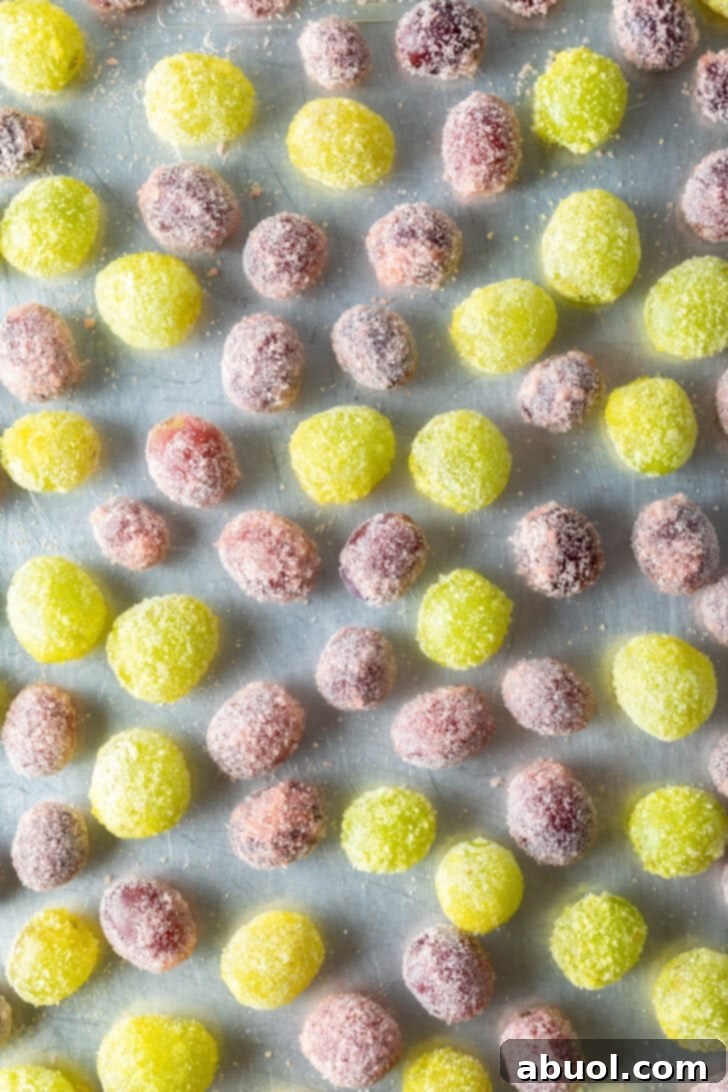 An overhead shot displaying a beautiful mix of green and purple candy-coated grapes, meticulously spread out on a baking sheet to chill.