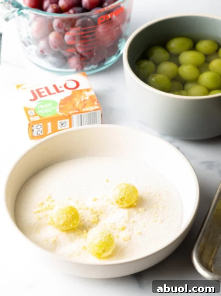 A shallow bowl captures three green grapes being meticulously rolled in a finely mixed sugar and Jell-O powder, ensuring an even coating.