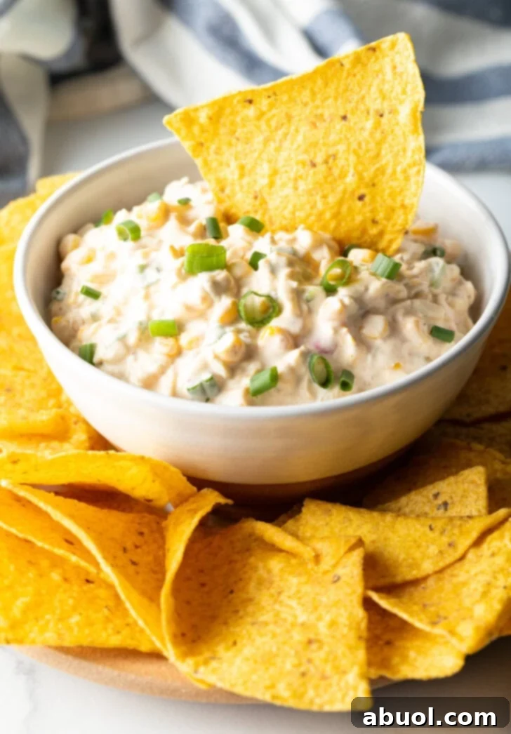 Tortilla chip scooping into a white bowl of creamy Mexican corn dip.