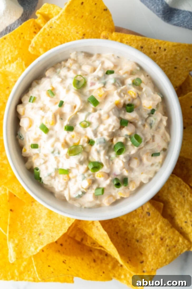 Top down view of a bowl of Mexican street corn dip topped with slices of green onion and surrounded by tortilla chips.