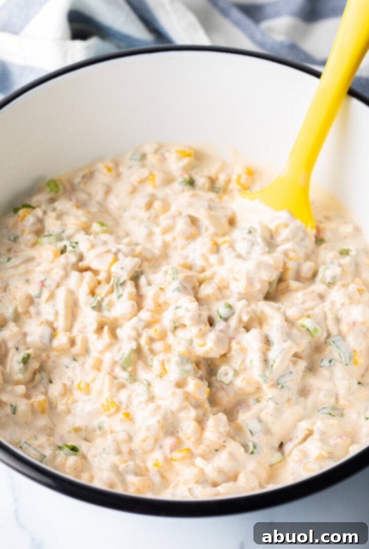 White bowl with yellow spatula mixing creamy corn dip.