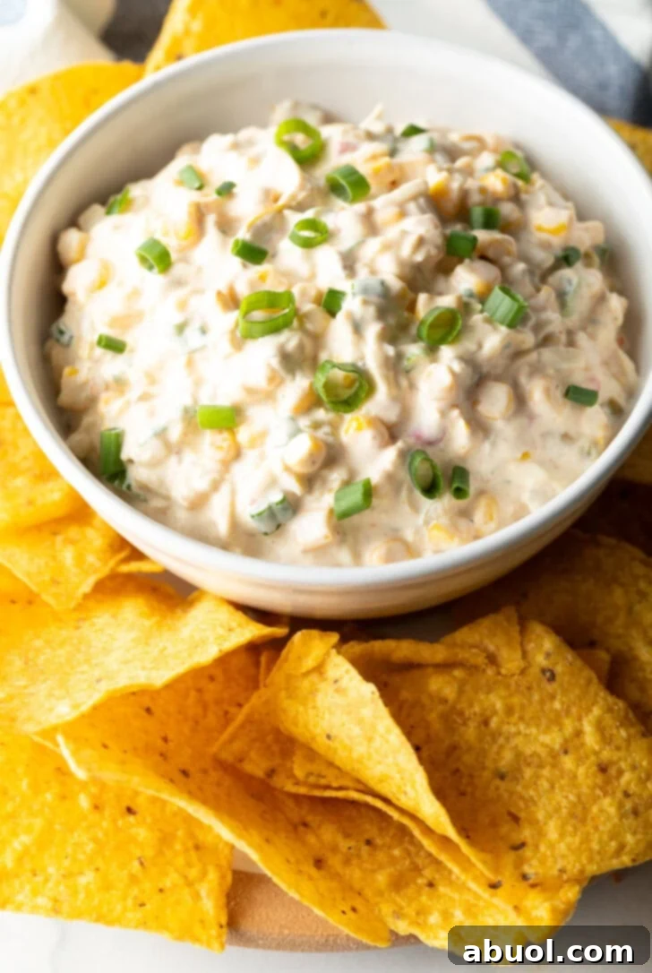 Top down view of a bowl of Mexican street corn dip topped with slices of green onion and surrounded by tortilla chips.