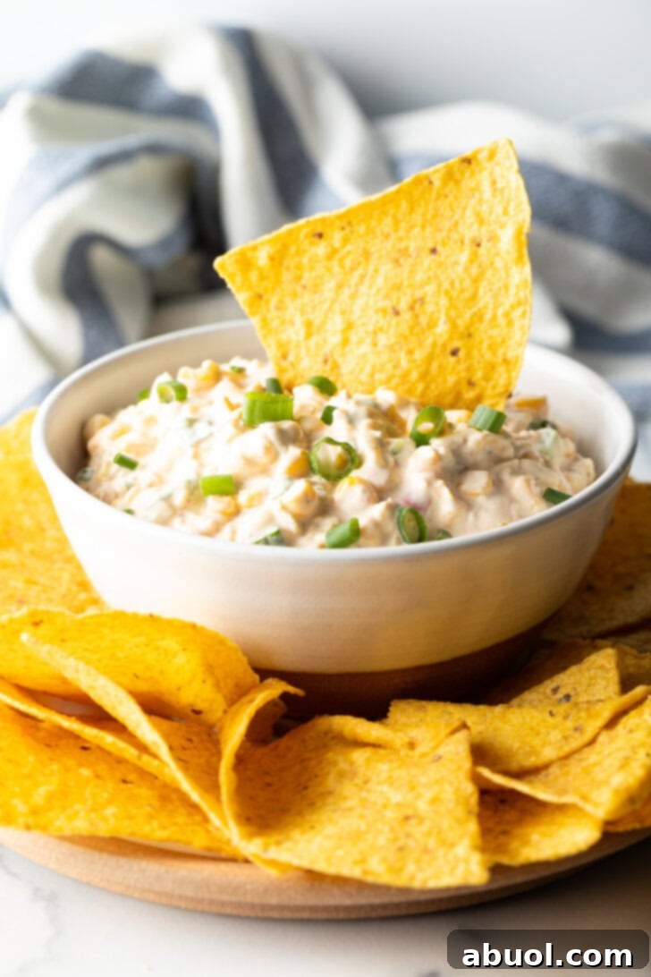 Tortilla chip scooping into a white bowl of creamy Mexican corn dip.