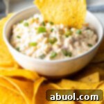 Tortilla chip scooping into a white bowl of creamy Mexican corn dip.