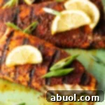 Close view of a fillet of grilled mahi mahi topped with a slice of lemon and green onions. A bite has been removed from the fish to show the white flaky inside of the meat.
