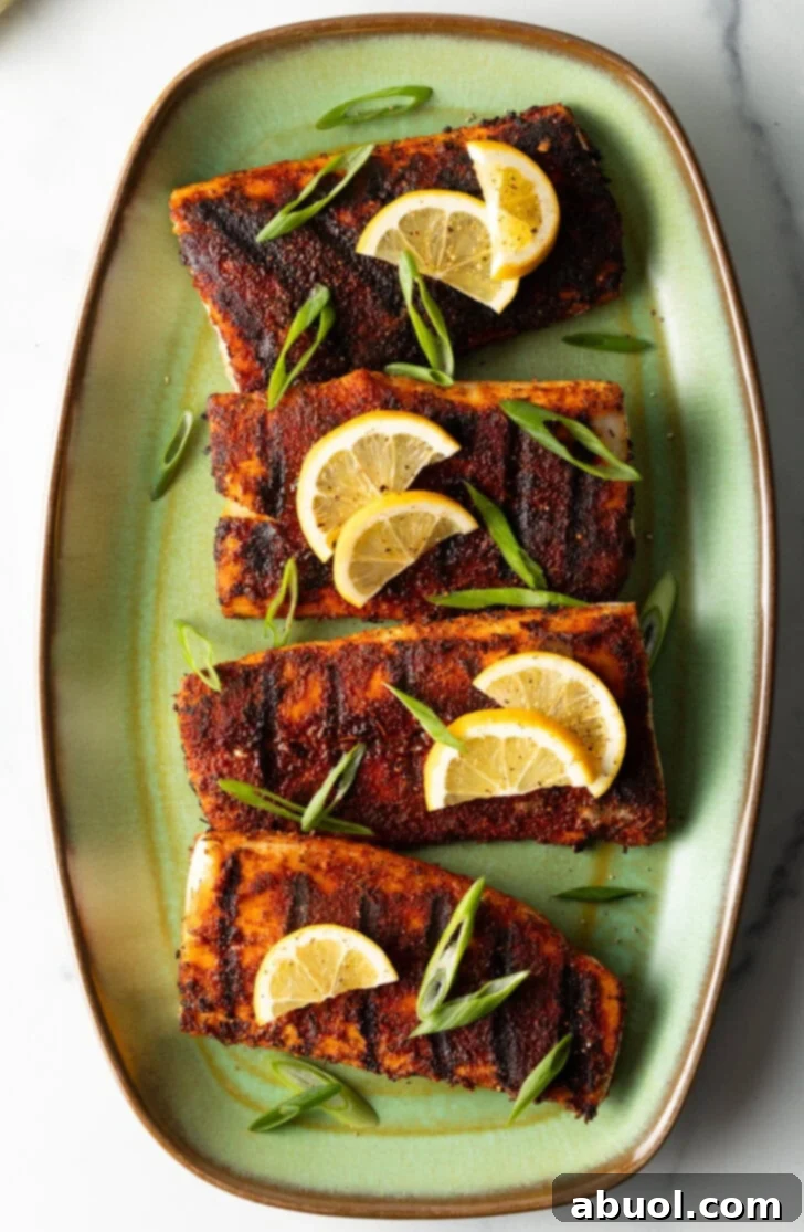 Top down view of 4 pieces of blackened and grilled fish, all topped with slices of lemon and green onions.