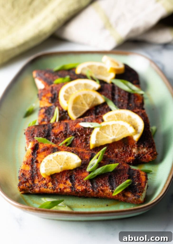 4 pieces of blackened and grilled fish, all topped with slices of lemon and green onions.