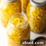 4 large jars of canned pickled banana peppers. The jar closest to the camera has the lid off showing the slices of peppers filling the jar.