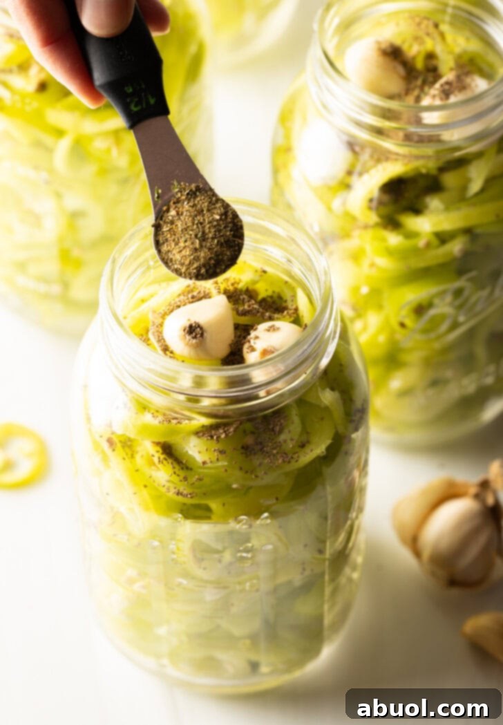 Adding spices to glass jars filled with pepper slices and garlic cloves.