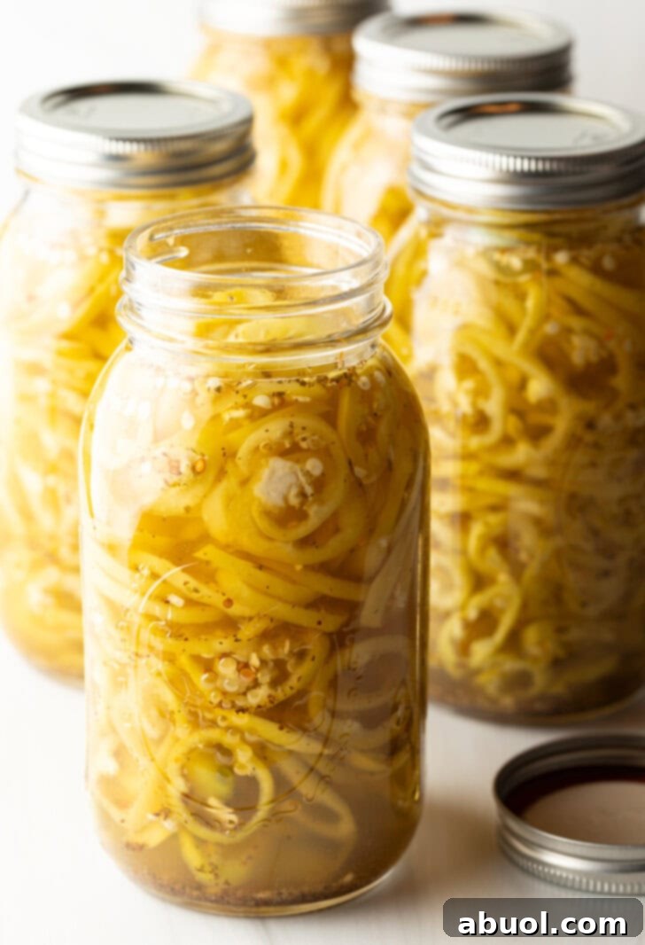 4 large jars of canned pickled banana peppers. The jar closest to the camera has the lid off showing the slices of peppers filling the jar.
