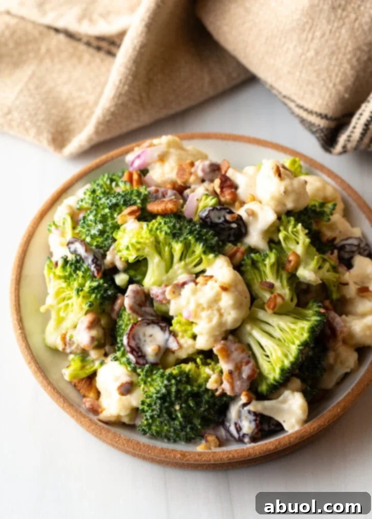 A large bowl of vibrant broccoli and cauliflower salad, beautifully tossed with toasted pecans, finely diced red onions, and ruby-red cranberries, ready to be served.