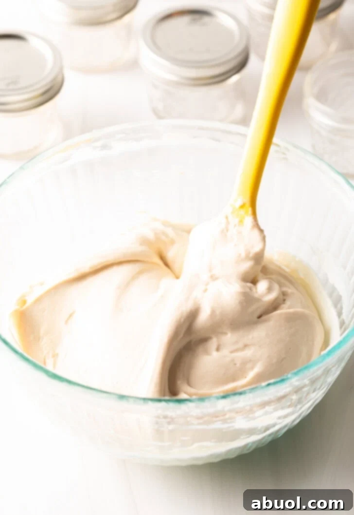 A vibrant yellow spatula expertly whipping a bowl of homemade protein yogurt, creating a perfectly smooth and creamy texture ideal for the protein pudding recipe. The motion highlights the ease of preparation.