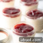 Five small glass jars of protein pudding topped with raspberry jam, illustrating the finished healthy snack or dessert.