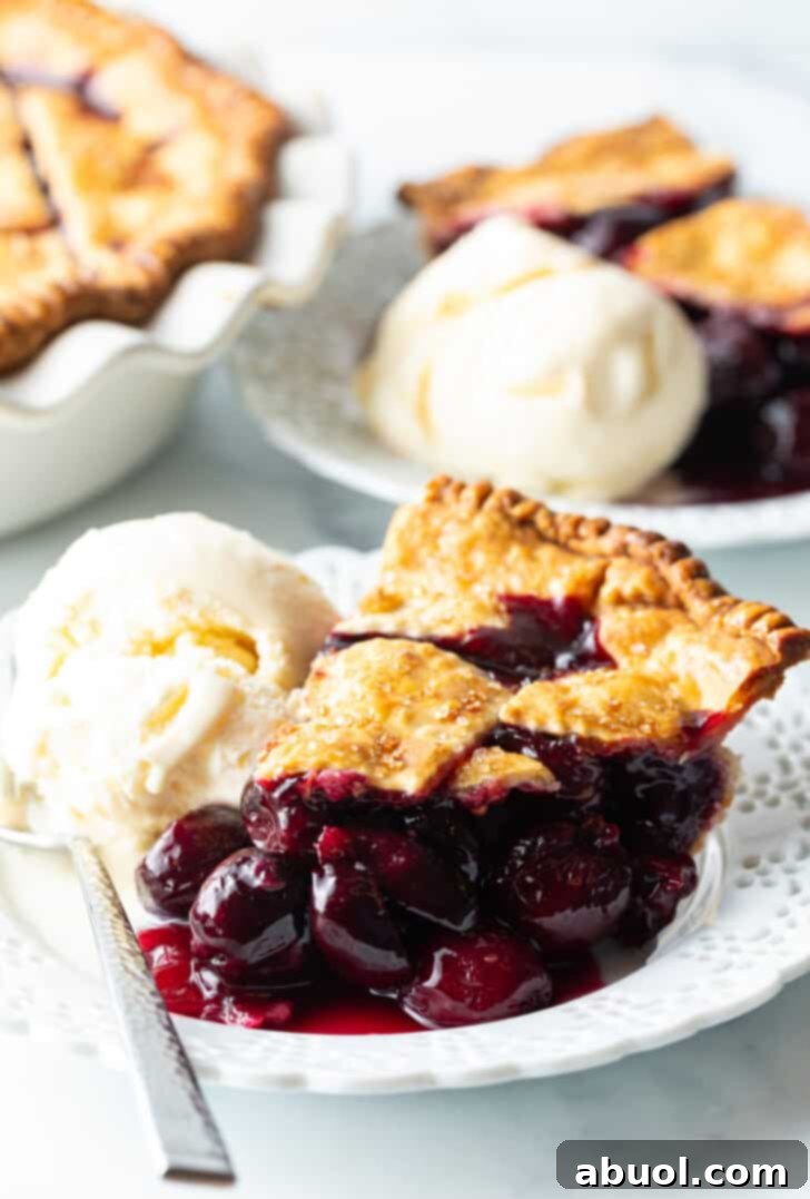 Slice of homemade cherry pie on a white plate, with scoop of vanilla ice cream on the side.
