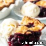 Slice of homemade cherry pie on a white plate, with scoop of vanilla ice cream on the side.