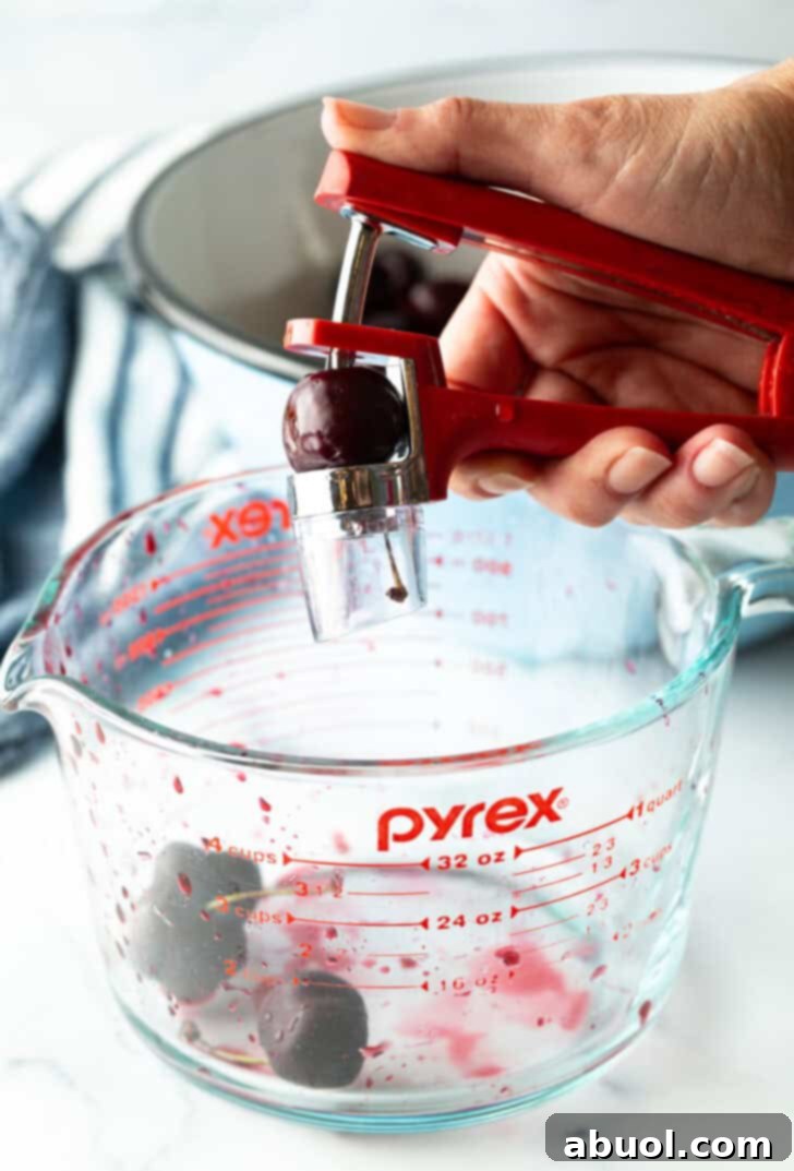 Hand using a cherry pitter to remove the pit from a fresh cherry.